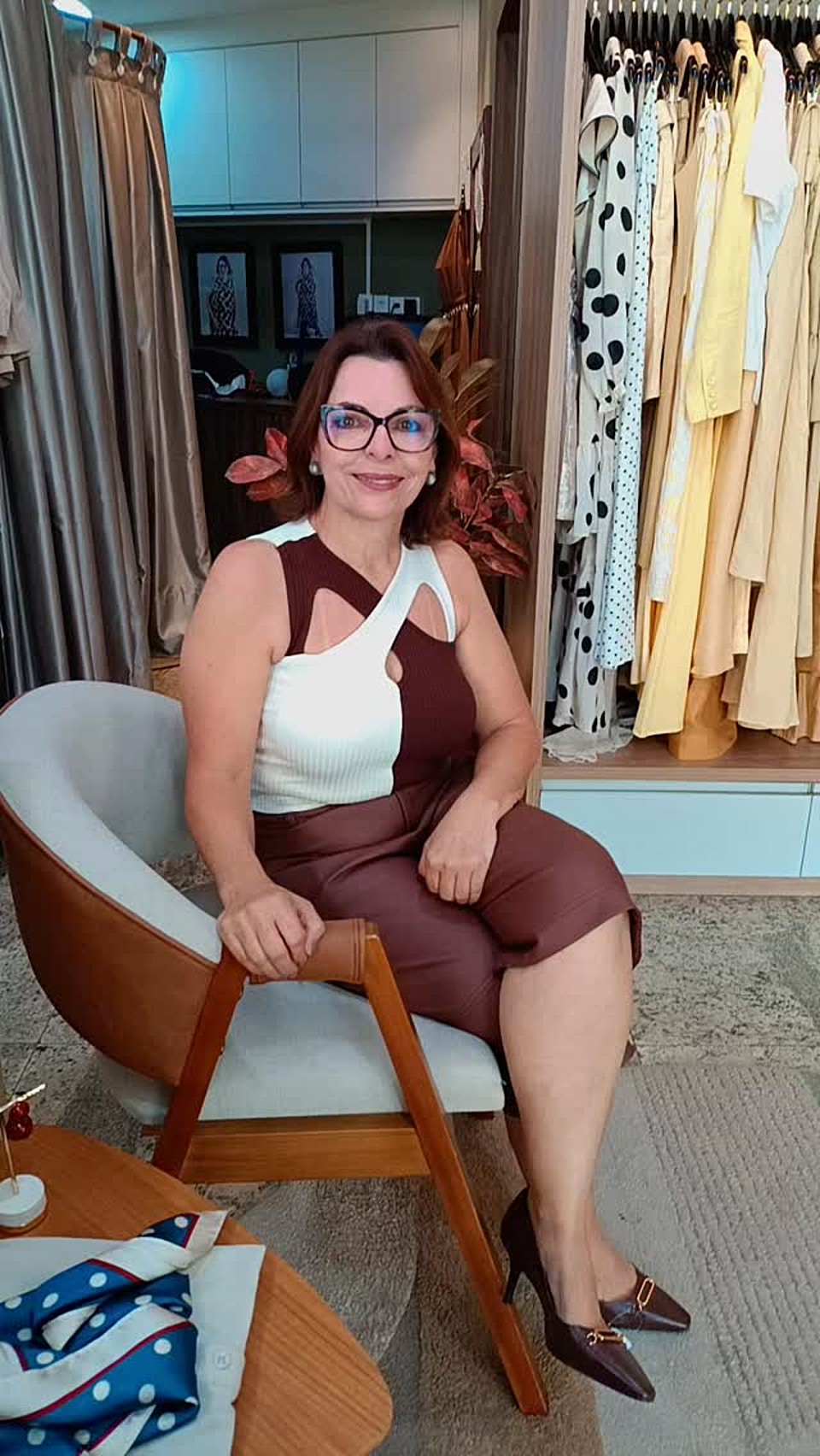 Arlene Germania sentada em uma poltrona na boutique, em frente às araras